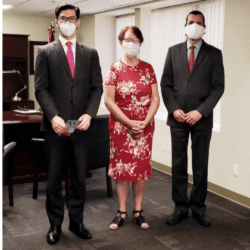 Three people in suits and masks stand next to a woman.