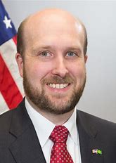 Man in suit with American flag background.