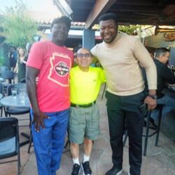 Three men smiling at outdoor restaurant.