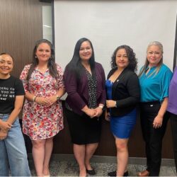 Seven women standing together in a room.