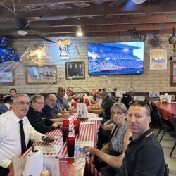 A group of people sitting at tables in front of a tv.
